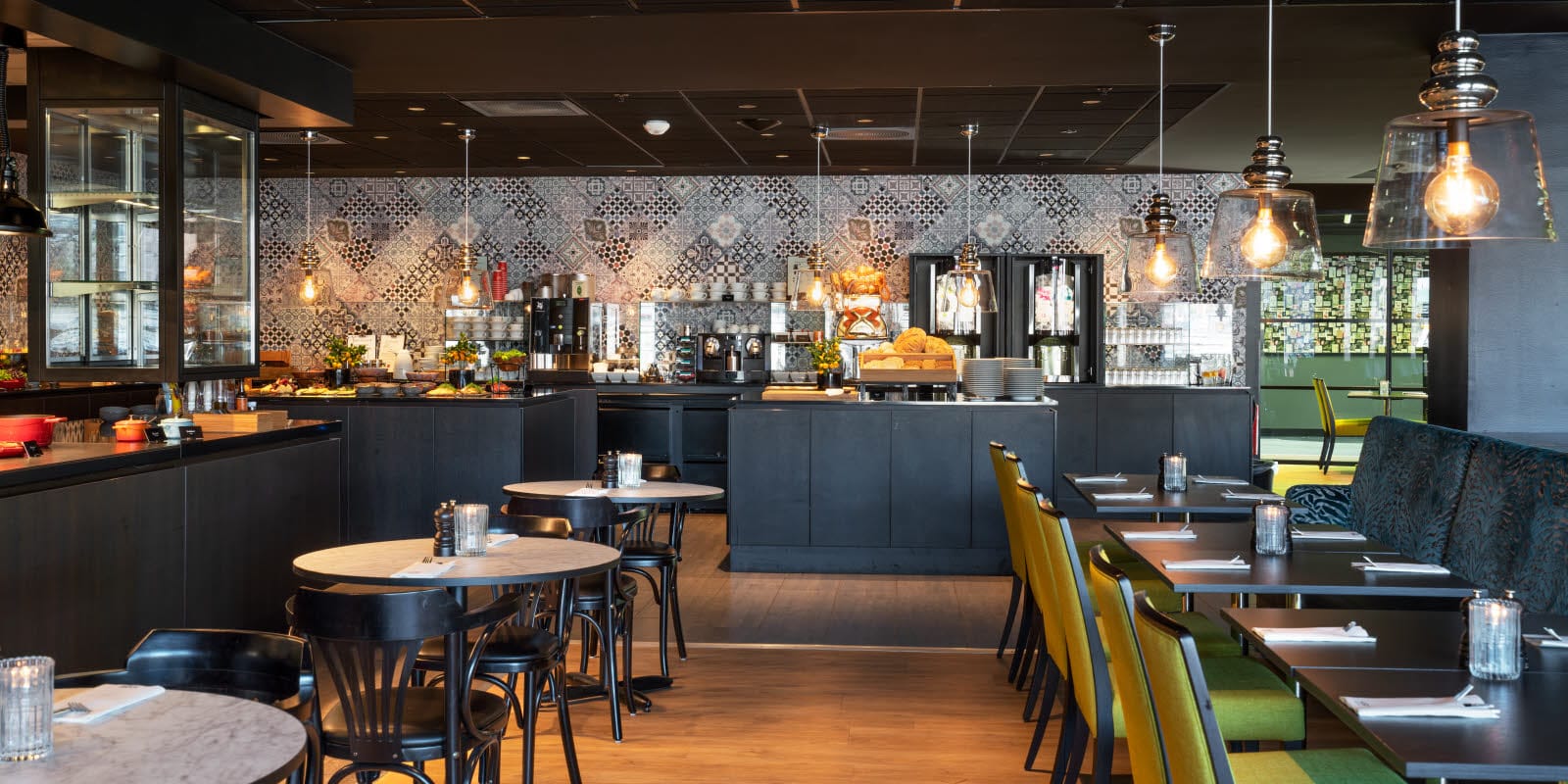 Restaurang med sittplatser som blickar mot kök och bufféområde med mönstrade kakelplattor på väggen på Thon Hotel Triaden i Lørenskog