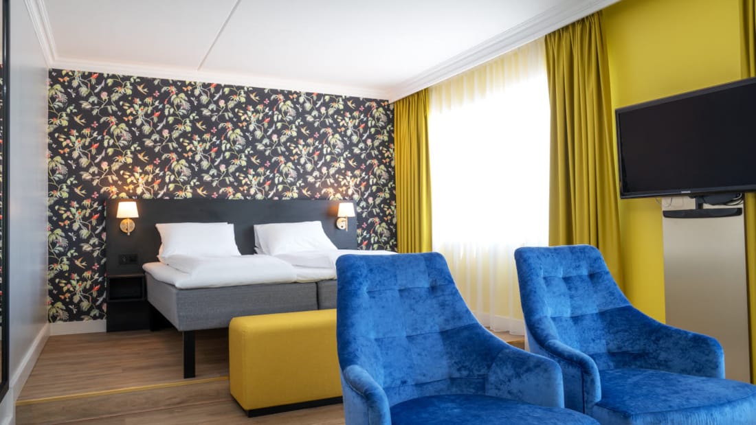Dobbeltseng, mønstret tapet, tv, to lenestoler og stort speil i buisness room på Thon Hotel Triaden i Lørenskog