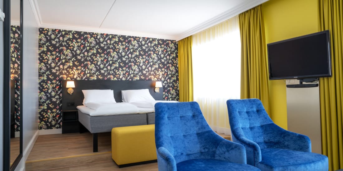 Dobbeltseng, mønstret tapet, tv, to lenestoler og stort speil i buisness room på Thon Hotel Triaden i Lørenskog
