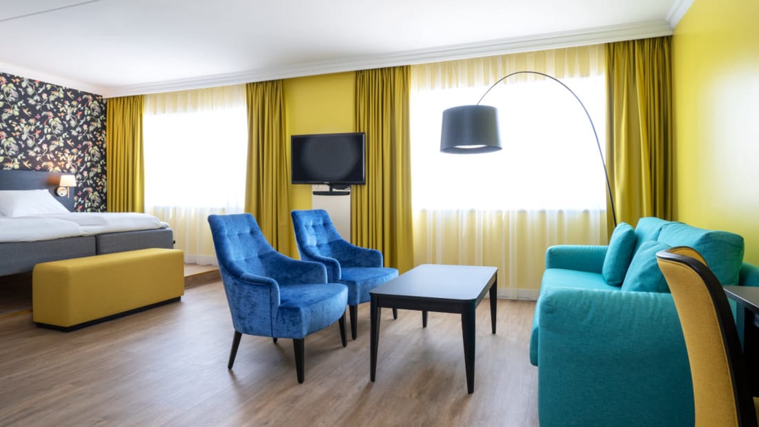 Dobbeltseng, mønstret tapet, tv, to lenestoler og sittegruppe i buisness room på Thon Hotel Triaden i Lørenskog