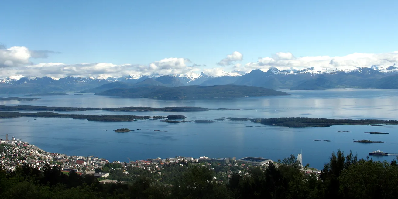 Molde sett fra oven med flotte fjell i horisonten, hvite skyer p&aring; himmelen og bl&aring;tt hav med bebyggelse i forkant.