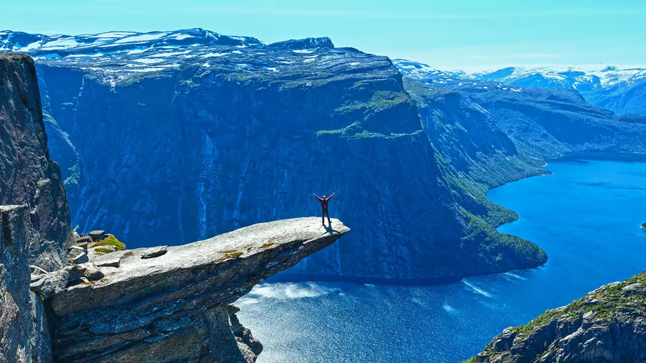 En person står ytterst på Trolltunga i strålende sol
