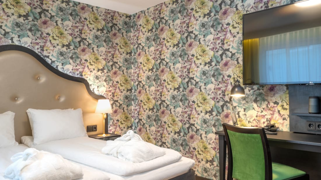 Blomstret tapet og dobbeltseng i dobbeltrom, gule gardiner, tv og arbeidsplass på Thon Hotel Cecil i Oslo sentrum