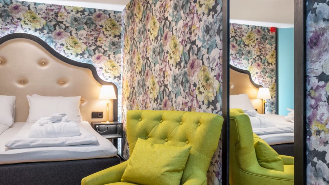 Blomstret tapet og stor dobbeltseng, grøn lænestol og spejl i superior-værelse på Thon Hotel Cecil i Oslo centrum