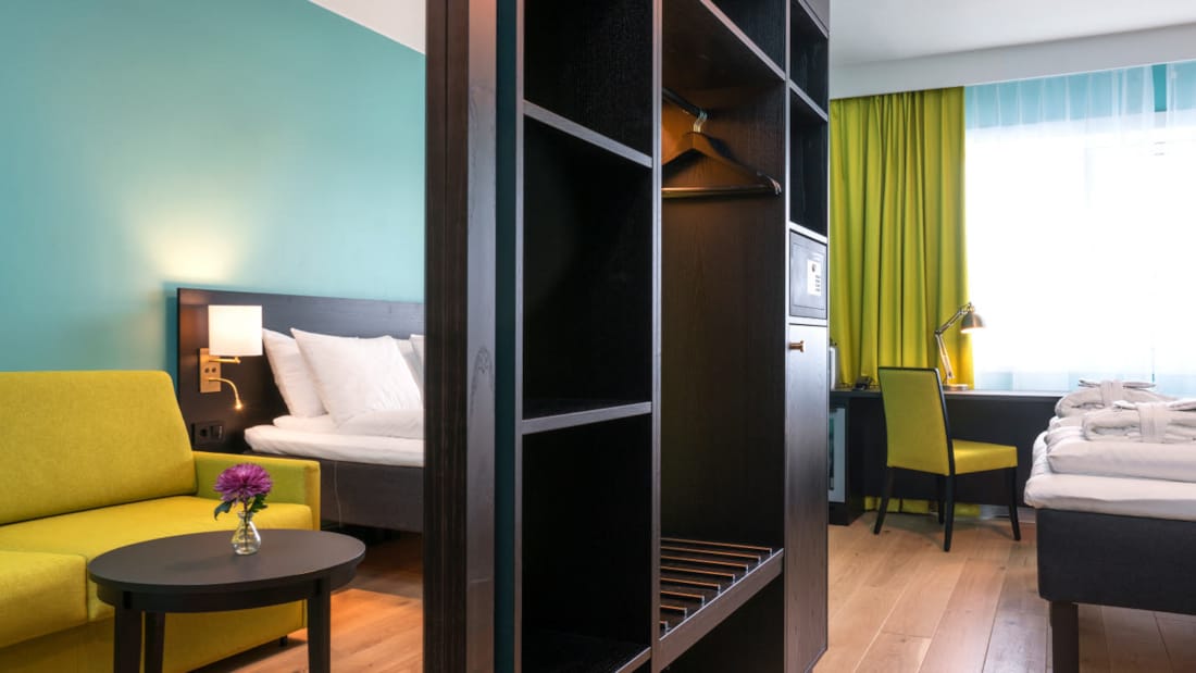 Gul soffa, garderob med spegel – säng och skrivbord på Thon Hotel Europa i Oslo centrum direkt vid slottsparken