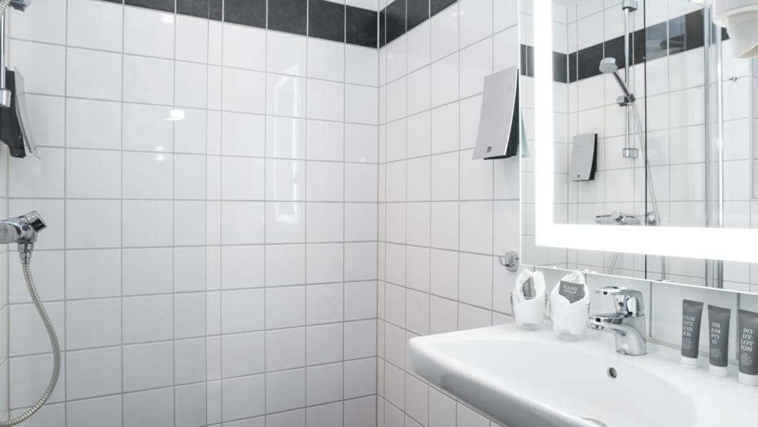 Badeværelse med bruser, spejl og håndvask på Thon Hotel Europa i Oslo centrum lige ved Slottsparken