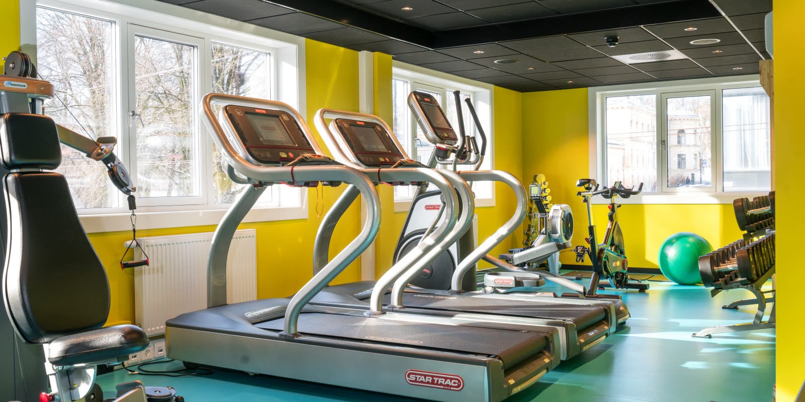 Gym med olika träningsredskap och gula väggar och turkost golv på Thon Hotel Europa i centrala Oslo precis vid Slottsparken