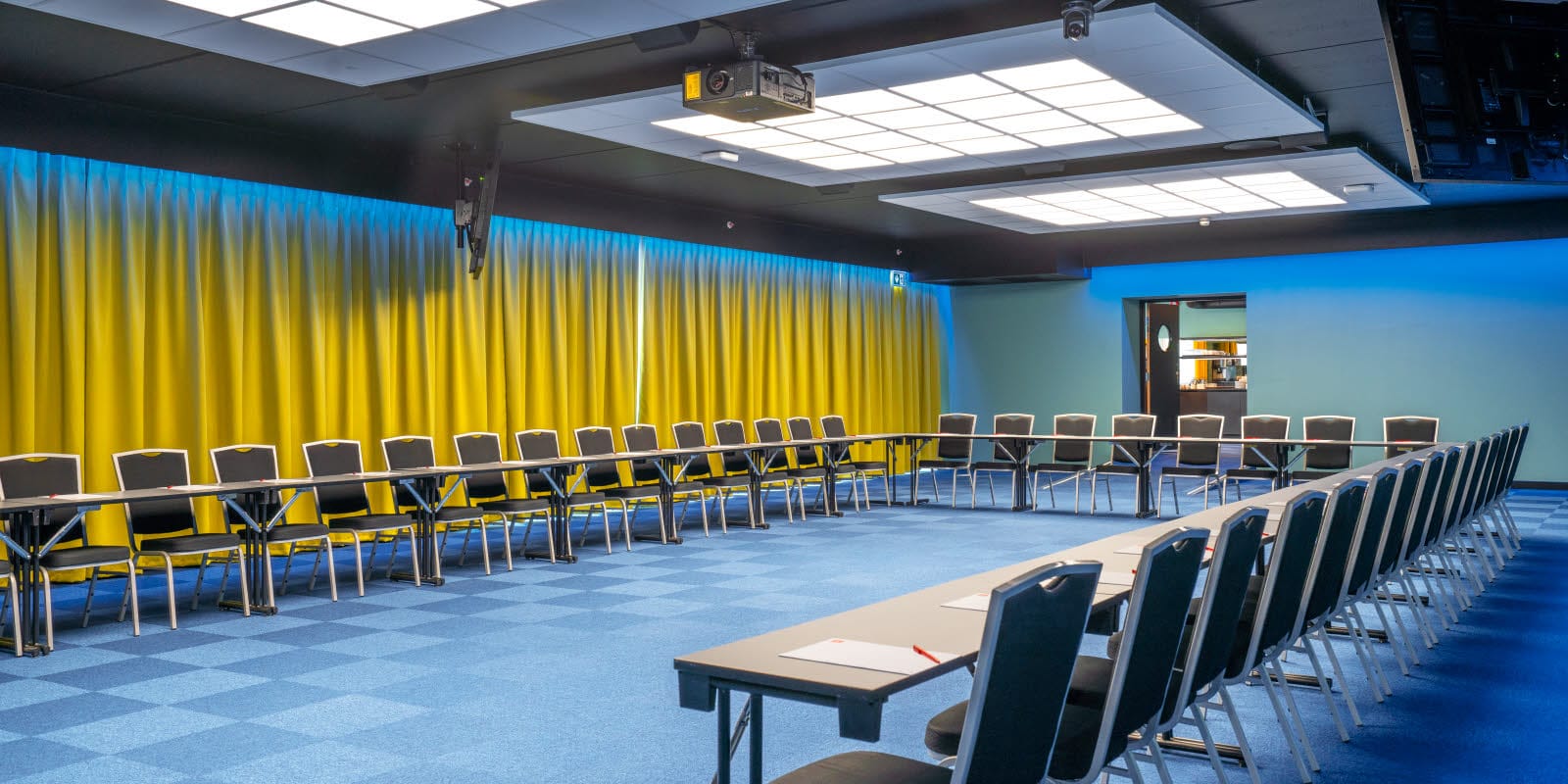 Konferenssal Bjerke med hästskomöblering med plats för 52 personer. Blå matta, gula gardiner och projektor på Thon Hotel Linne i Oslo