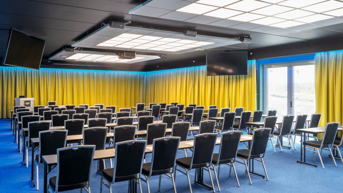 Konferencesal Bjerke med klasseværelse-opsætning med plads til 100 personer. Blåt tæppe, gule gardiner og projektor på Thon Hotel Linne i Oslo