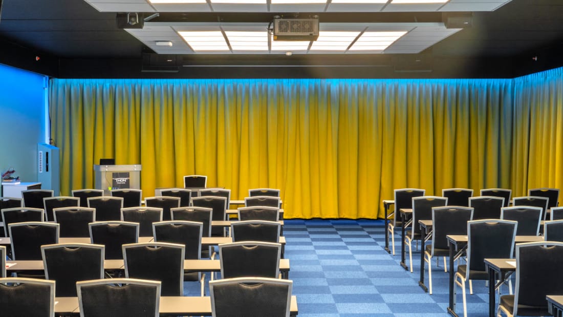 Konferencesal Bjerke med klasseværelse-opsætning med plads til 100 personer. Blåt tæppe, gule gardiner og projektor på Thon Hotel Linne i Oslo