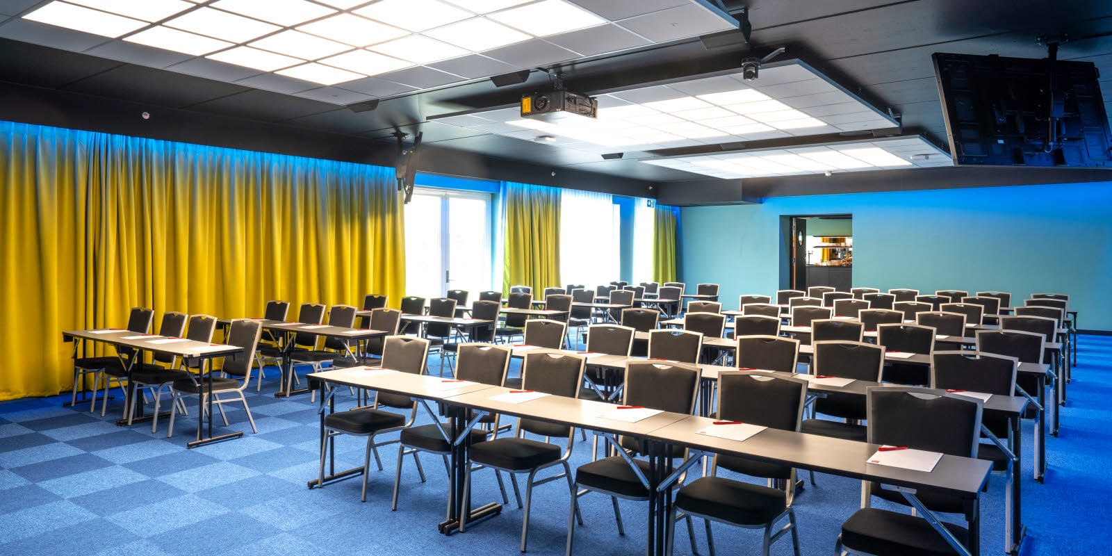 Konferenssal Bjerke med klassrumsmöblering med plats för 100 personer. Blå matta, gula gardiner och projektor på Thon Hotel Linne i Oslo