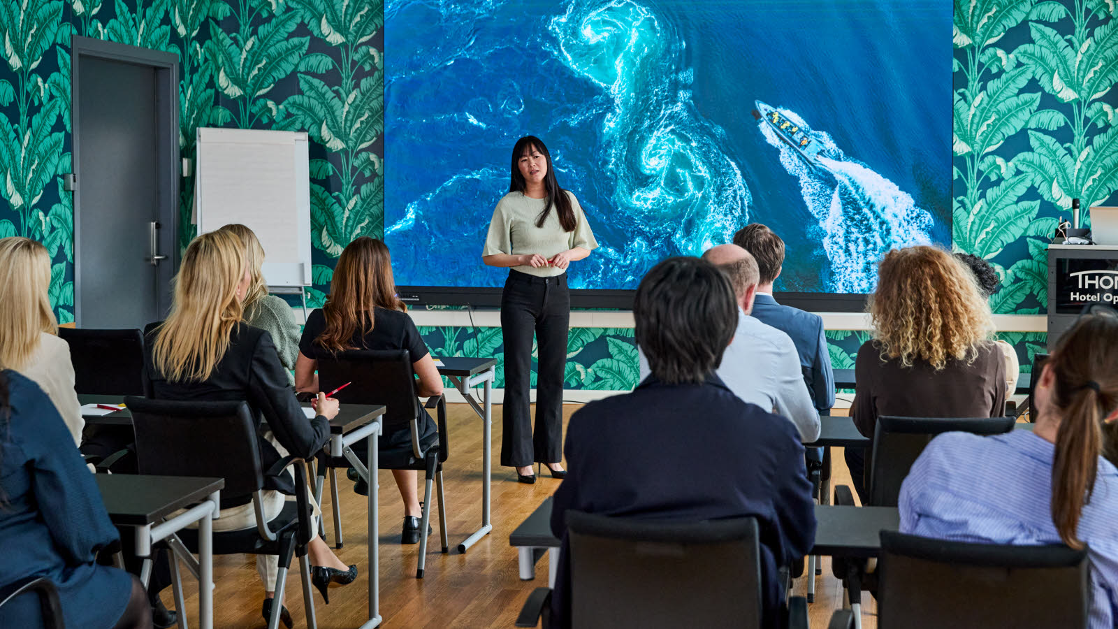 Fyldt konferencesal, foredragsholder og lærred.