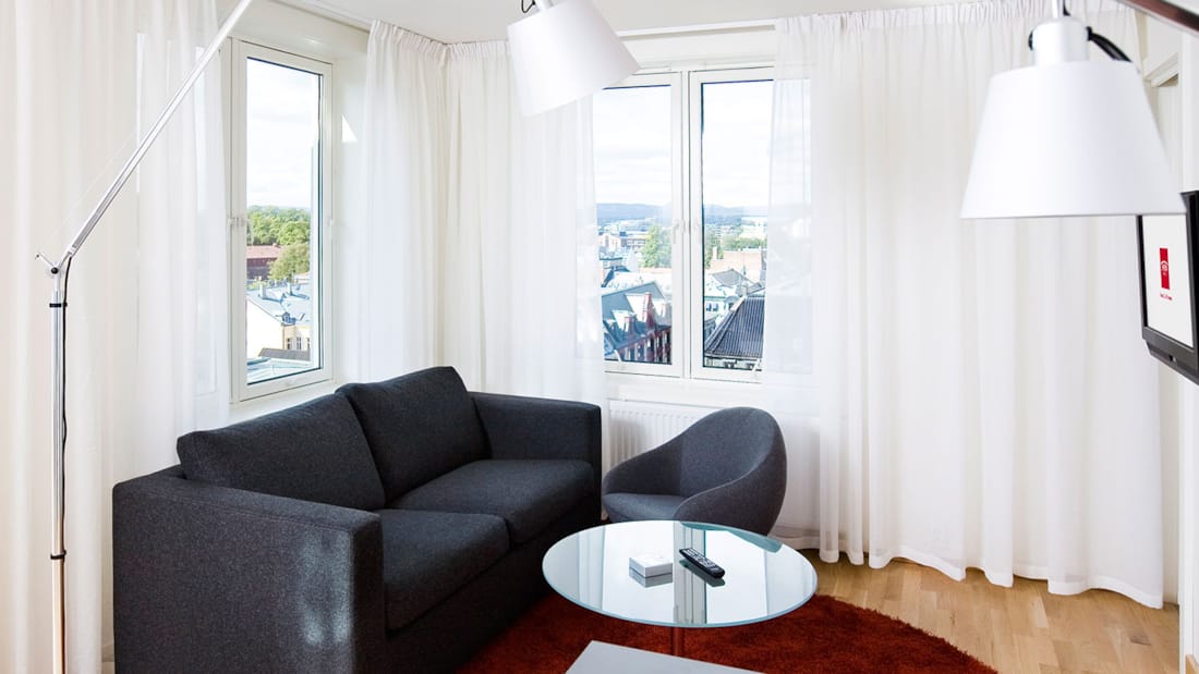 standard room triplefamily familierom stueseksjon med sofa, sofabord, lenestol, vegghengt tv, stålampe, parkettgulv, balkong med utsikt over Oslo sentrum