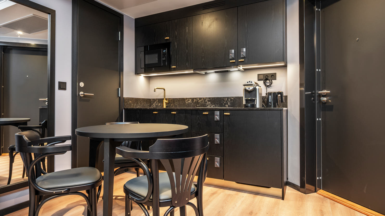 Stort hotellrom med rund spisebord og spisestoler og et lite kjøkken.