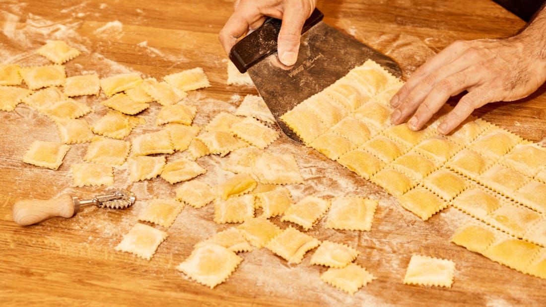 To hender som kutter opp hjemmelaget pasta på en trebenk på restauranten Osteria della Nonna