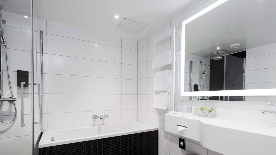 badrum med dusch, badkar, handdukshängare, upplyst spegel, handfat