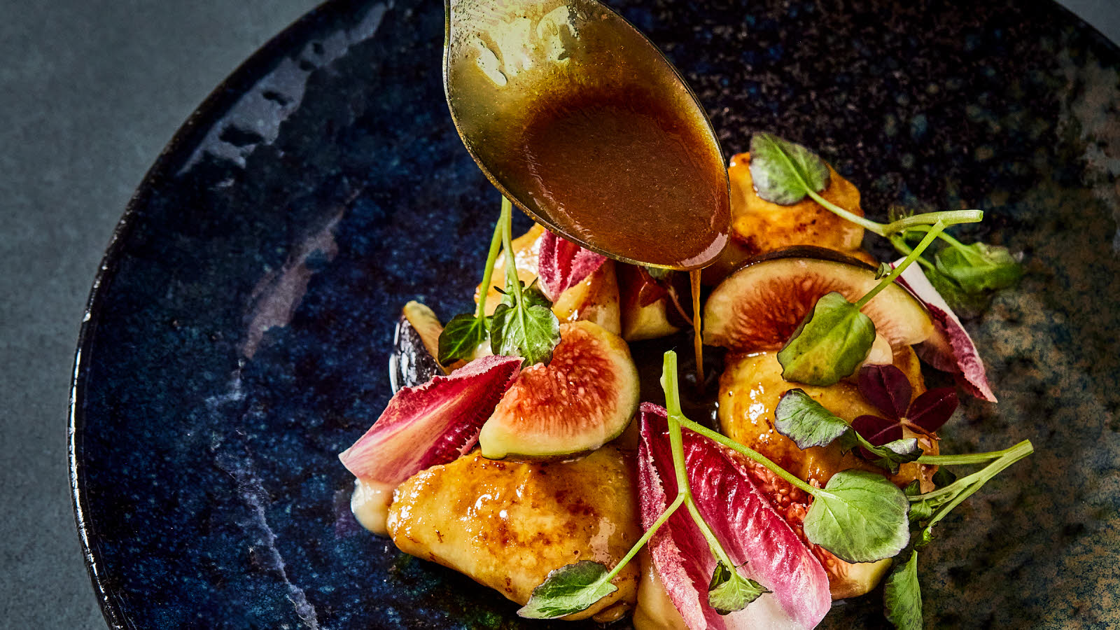 Section of a plate with figs, different types of lettuce. Tablespoon pouring brown gravy over the dish.