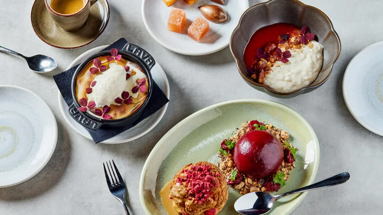 Utsnitt av flere småretter og desserter på et bord med lys duk, sett ovenfra.