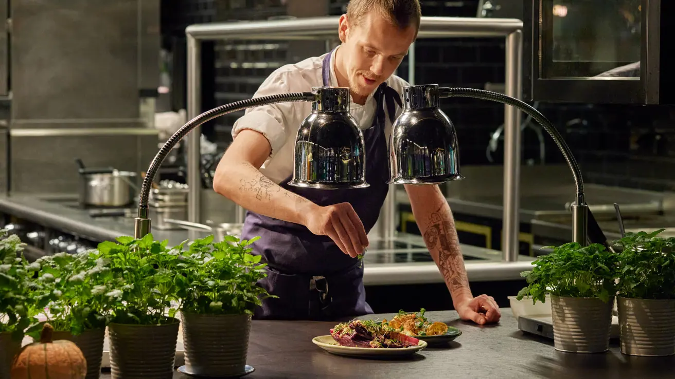 Kokk som lager mat bak en kjøkkenbenk på et åpent kjøkken, sett fra restauranten.