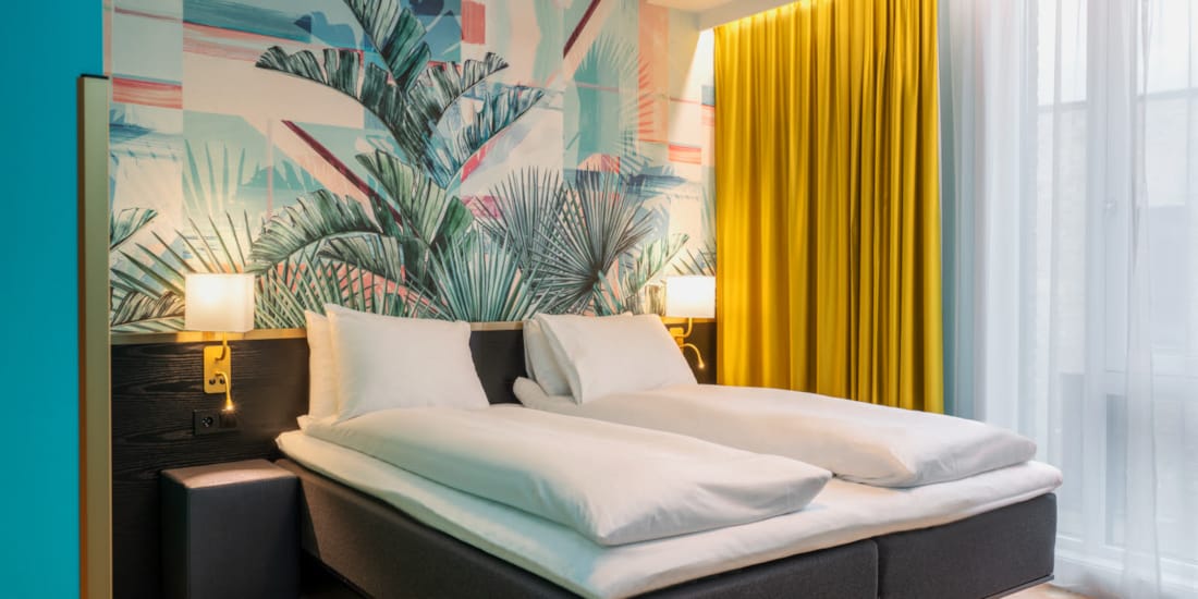 Dobbeltseng og fargerik palmetapet i standard HCP rom på Thon Hotel Storo
