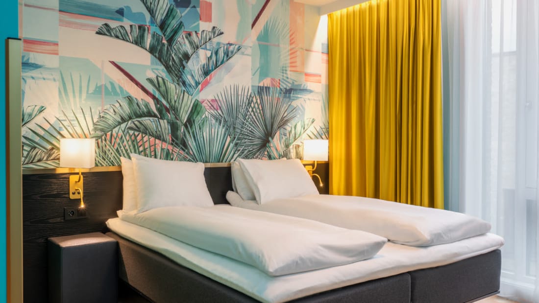 Dobbeltseng og farverigt palmetapet i standard HCP værelse på Thon Hotel Storo