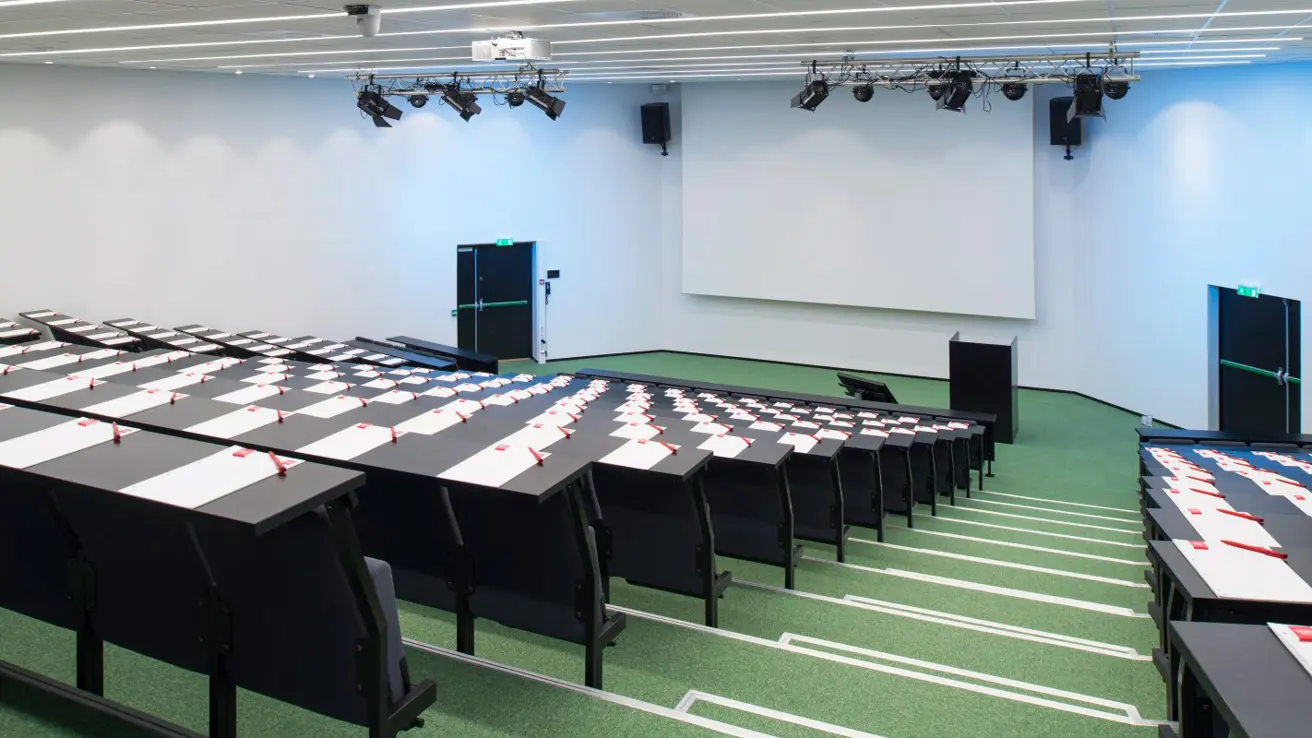 Conference room atrium, raised rows of chairs and tables with stairs, large screen in front