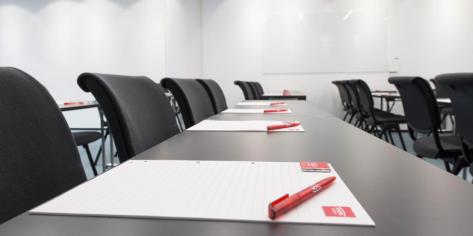 detaljbilde av konferansestoler og bor på rekke med notatblokker og penn
