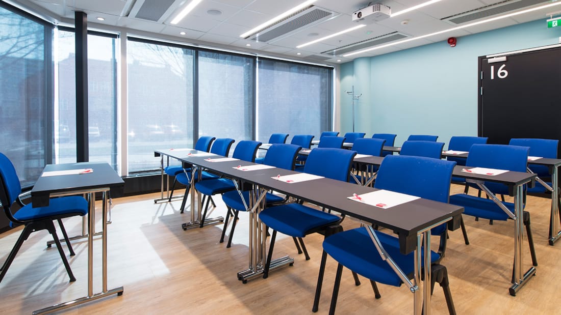 konferensrum midstuen, detaljbild av stolar och bord med klassrumsmöblering med bord längst fram, fönster som släpper in ljus i rummet, parkettgolv