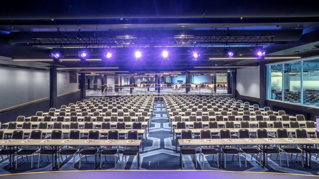 Großer Konferenzraum in Klassenzimmerbestuhlung, Scheinwerfer und Bühne mit Beamer
