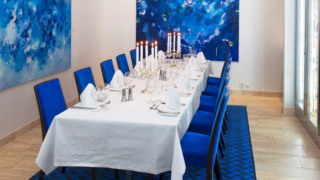 Mødelokale med langbord med blå stole og malerier på væggen