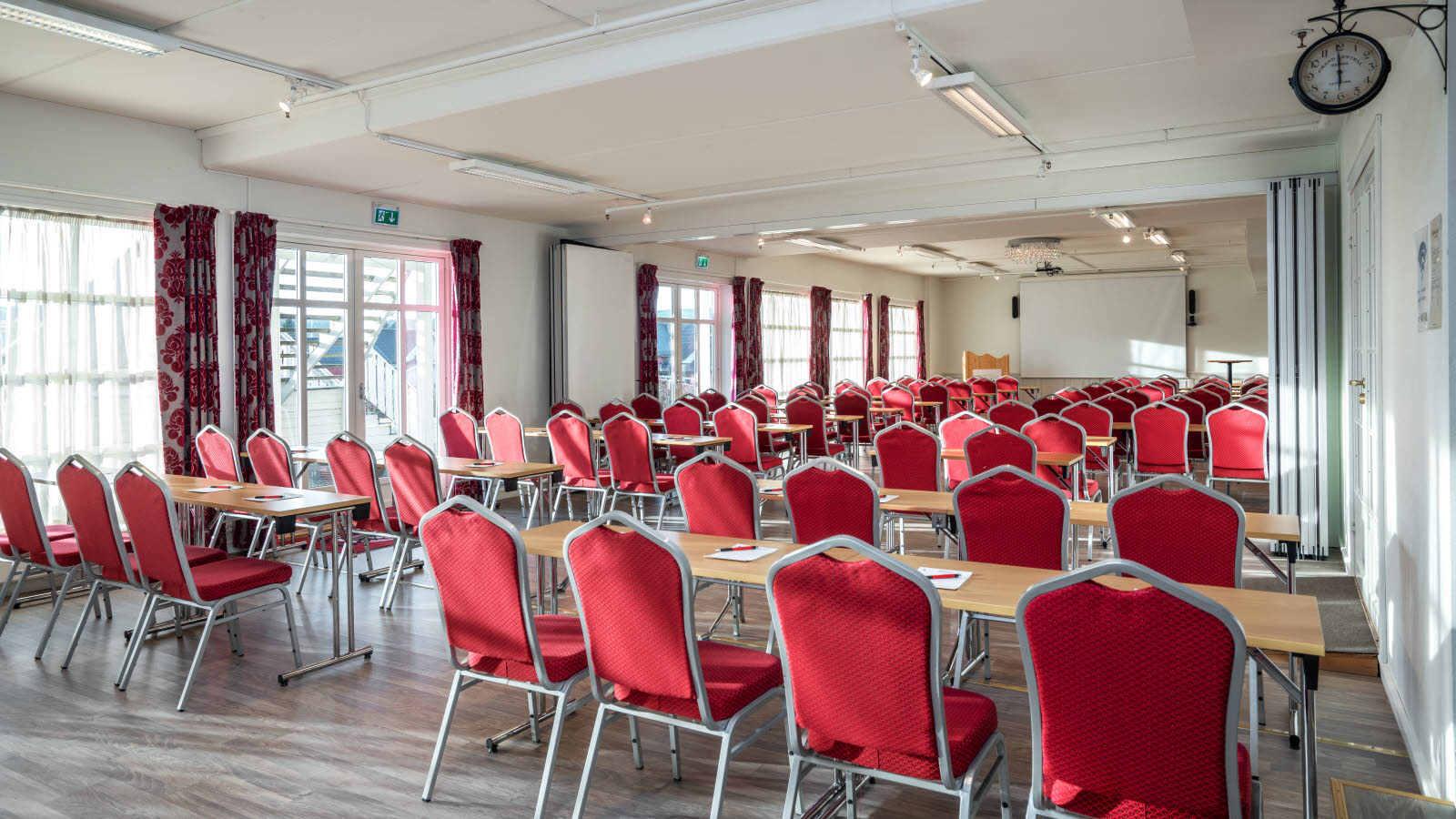 Lyst møterom med store vinduer på venstre side. Bord og røde stoler i klasseromsoppsett.