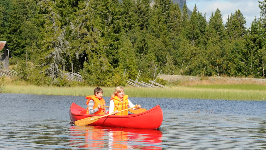 To mennesker, som padler i en rød kano i solskin