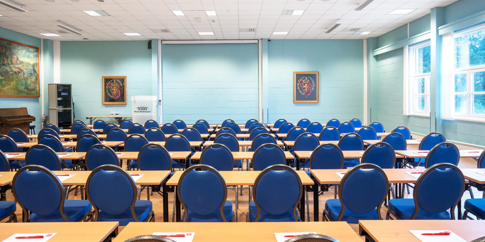 Konferanserom Olav bestående av rader med blå stoler og bord i et lyst blått moderne konferanselokale