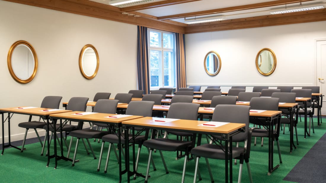Skeikampen mødelokale hvidt lokale med rækker med mørke stole og lyse borde og grønt gulv