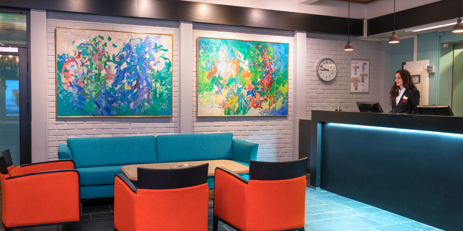 Rezeption (mit Personalbetreuung) mit Sofa und Sitzgelegenheiten. Große abstrakte Bilder an der Wand mit stimmungsvoller Beleuchtung im Thon Hotel Skeikampen