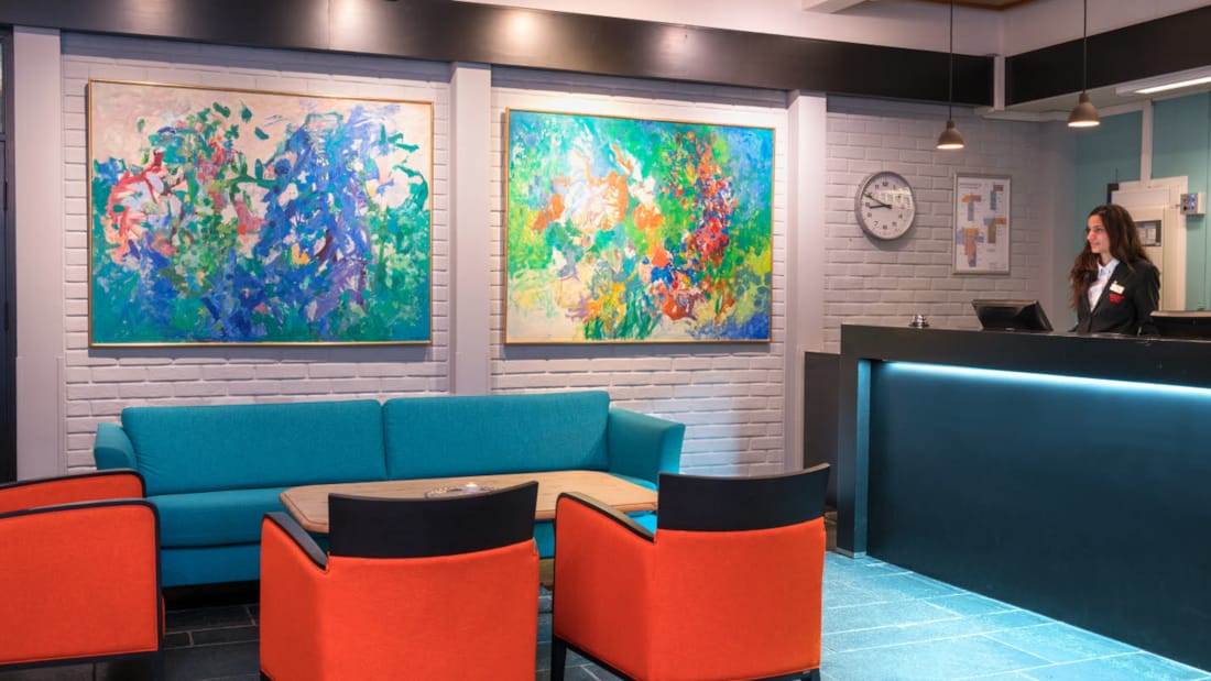 Bemannad reception med soffa och sittplatser och stora abstrakta tavlor på väggen med dov belysning på Thon Hotel Skeikampen