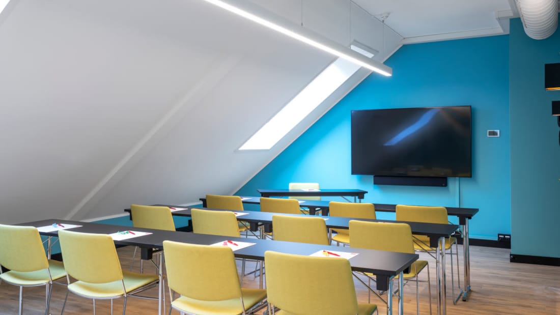Salle de réunion avec plafond en pente en configuration salle de classe et TV au mur