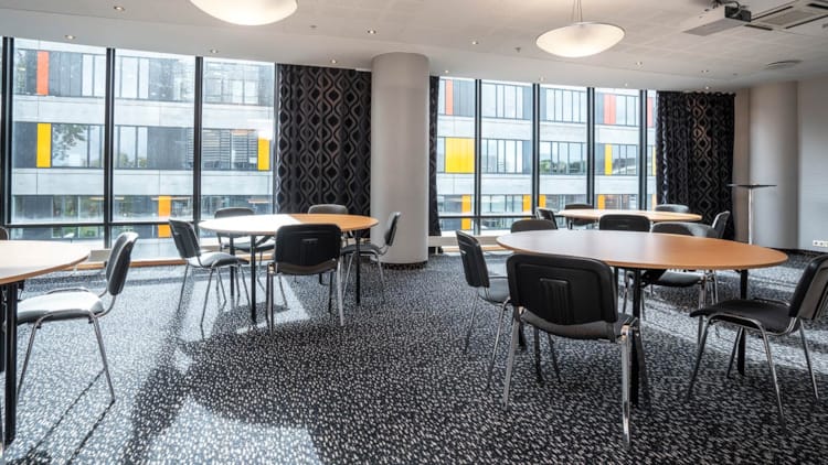 Mødelokale med runde borde, projektor og store vinduer