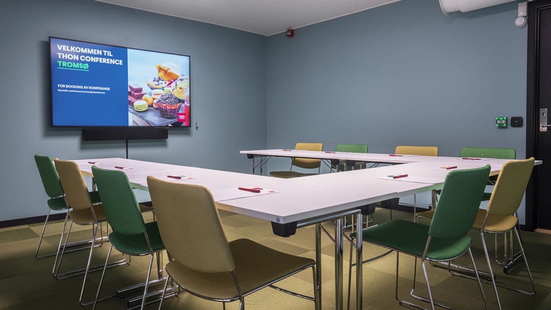 Mødelokale i u-bordsopsætning med stole og væghængt tv