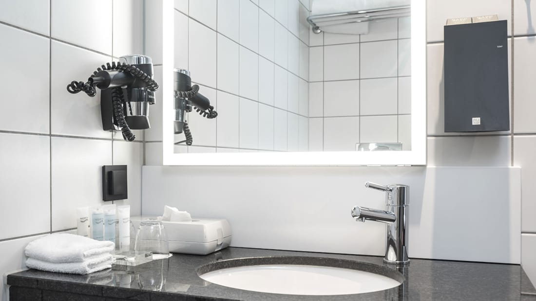 Badeværelse med håndvask, spejl, hårtørrer og toiletartikler på Thon Hotel Tromsø