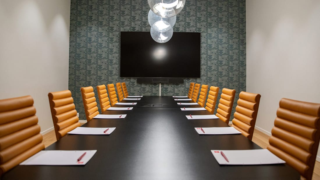 Konferensrum möblerat med stort bord med stolar och vägghängd TV