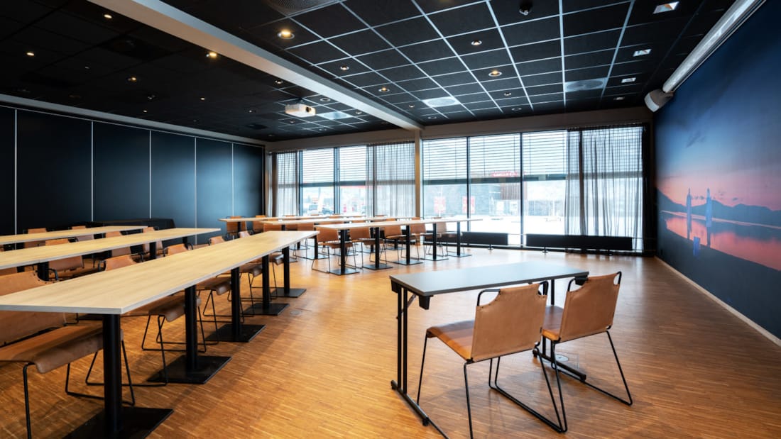 Salle de réunion Mor Åse dans un agencement de salle de classe avec un bureau avec deux sièges à l’avant, des fenêtres sur tout le petit côté.