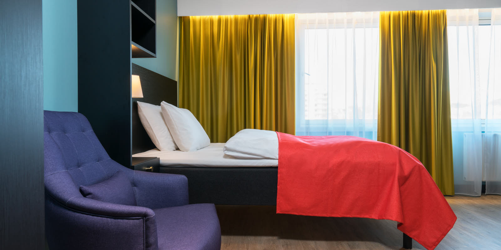 Tweepersoonsbed en blauwe leunstoel in eenpersoonsappartement van Thon Hotel Linne Apartments