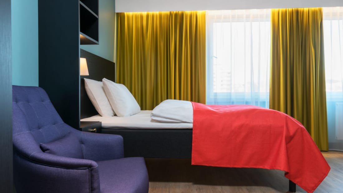 Tweepersoonsbed en blauwe leunstoel in eenpersoonsappartement van Thon Hotel Linne Apartments