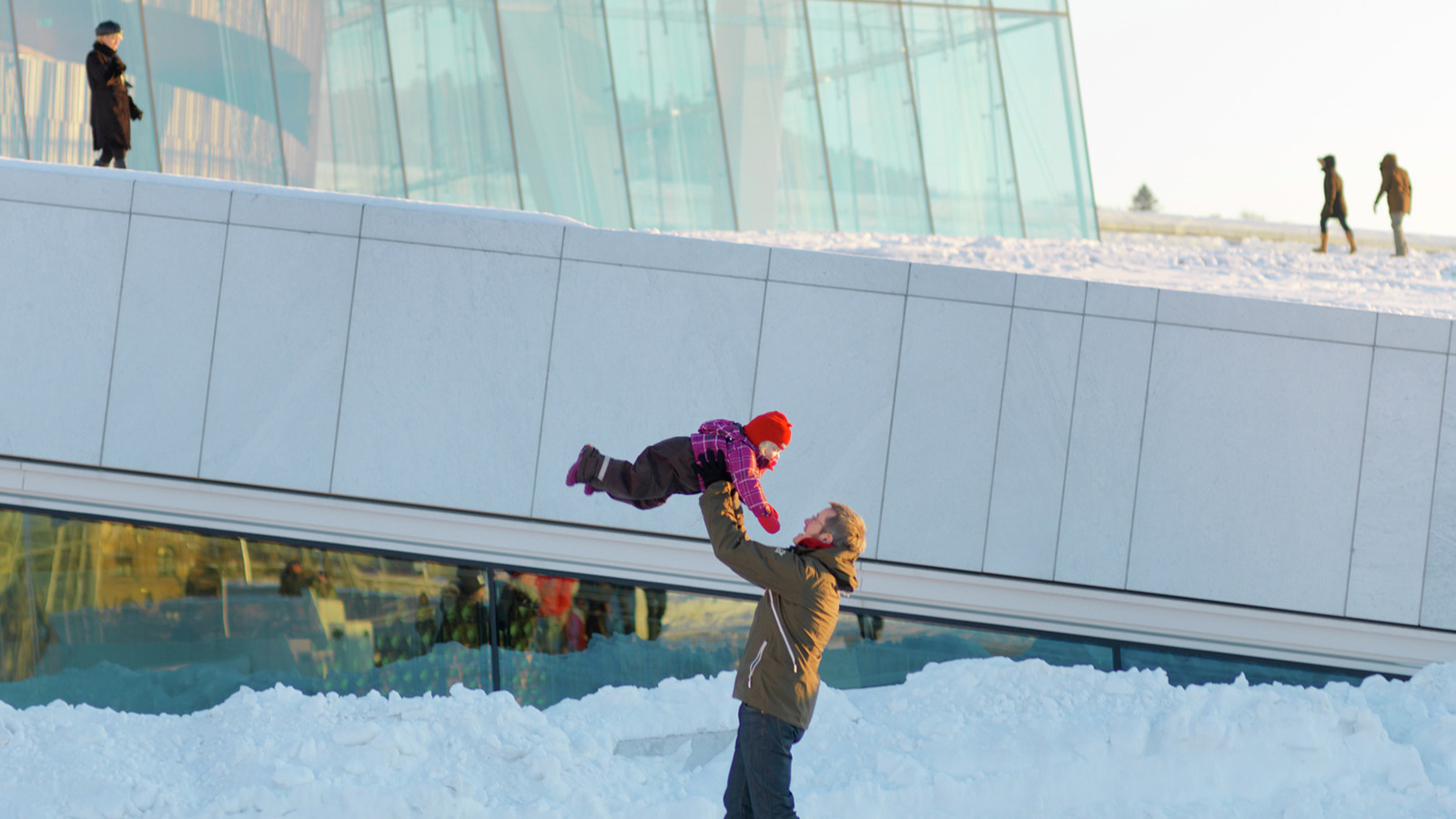 Men man løfter et barn uten for Operaen. Bakken er dekket av snø.