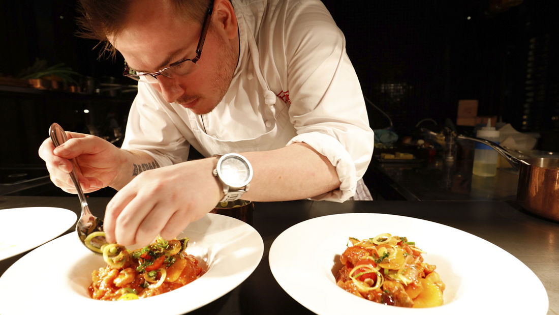 A chef at Paleo Arctic preparing bacalao with pickled borettane onion and olives.