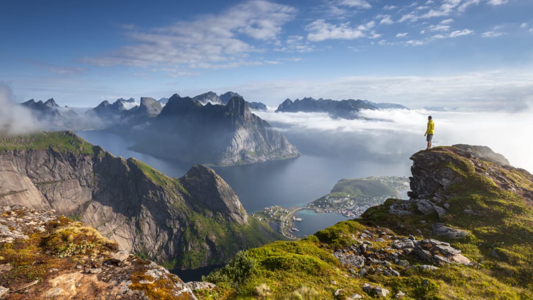 Persoon die op de top van een berg staat en uitkijkt over de Lofoten