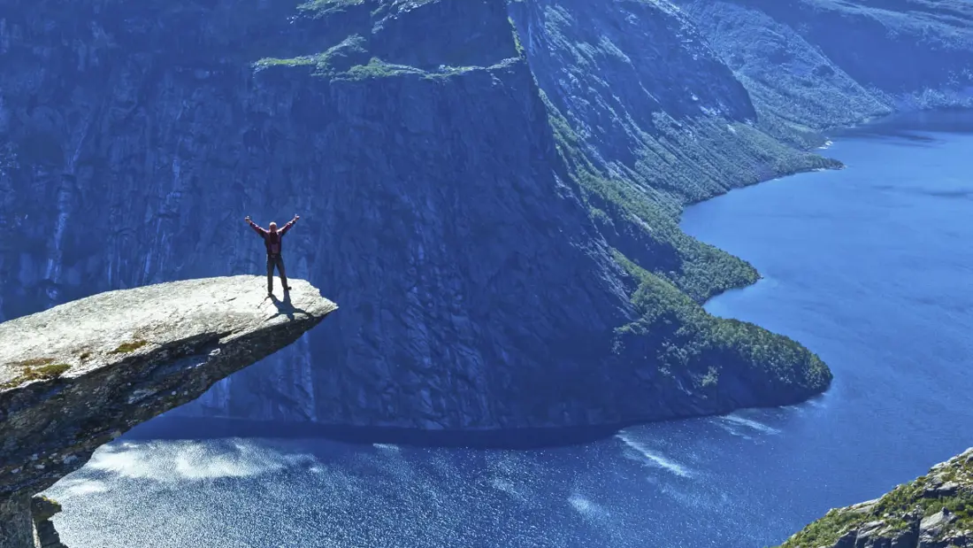 Person på Trolltunga foran fjorden under en blå himmel