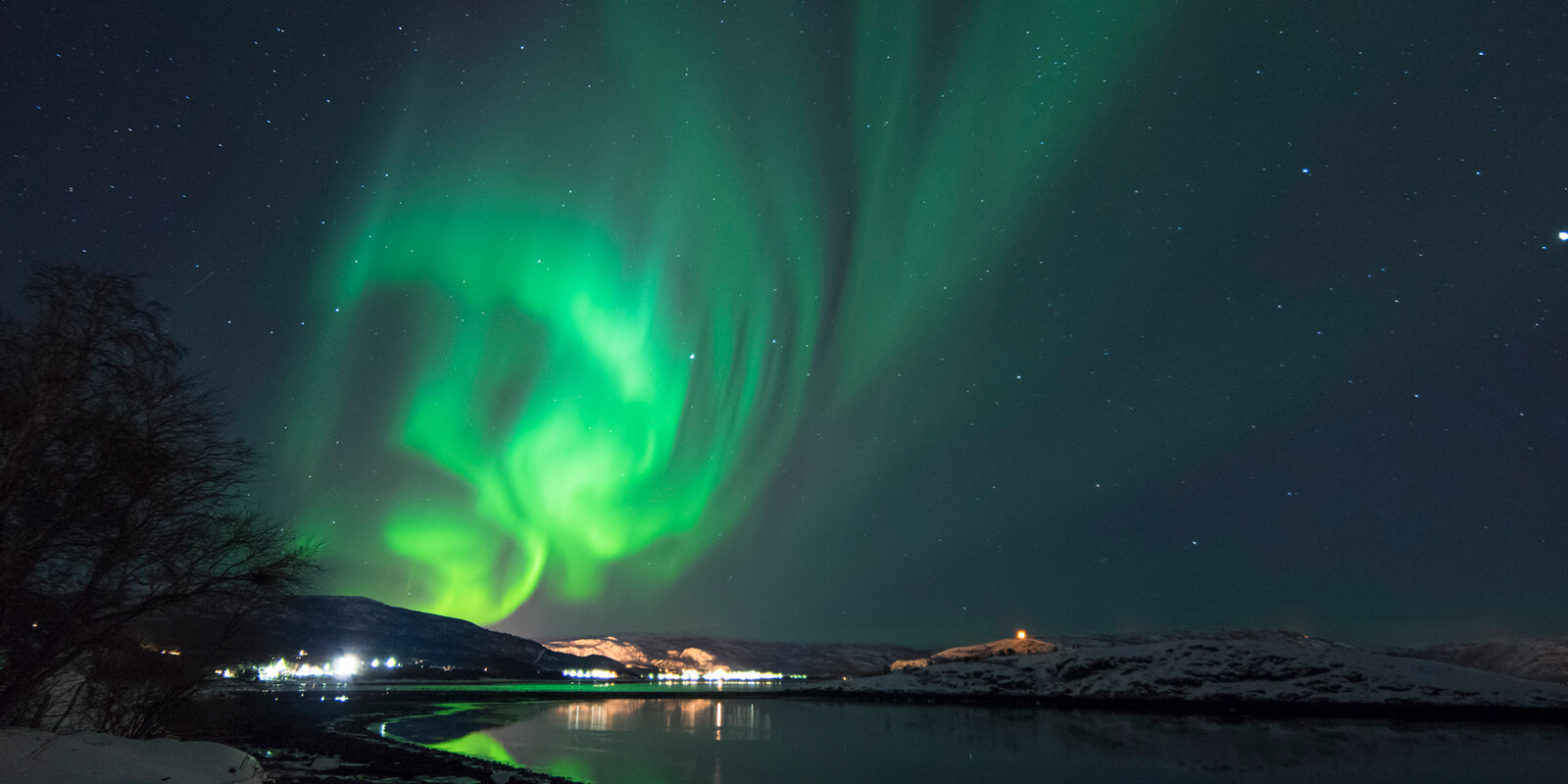 Nordlys som lyser over vann og fjell i vintermørket i Hammerfest