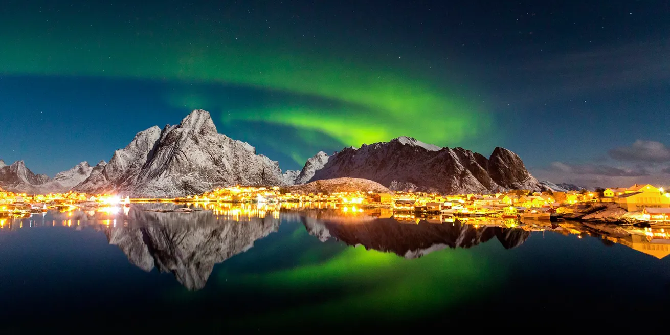 Les aurores boréales dansent dans les Lofoten au-dessus des montagnes et illuminent la ville dans l’obscurité en faisant éblouir l’océan.